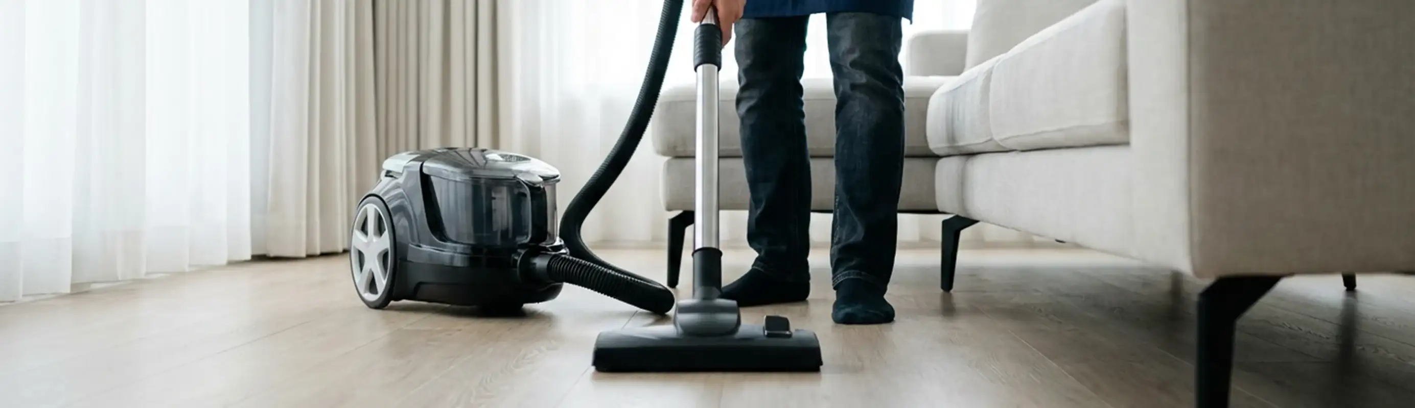 Professional house cleaner vacuuming a living room floor with a canister vacuum cleaner, Erie, PA.