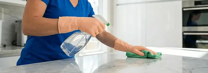 Maid service worker spraying and wiping a kitchen countertop with a microfiber cloth for sanitizing, Erie, PA.