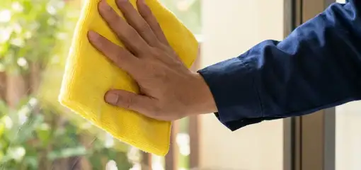 House cleaner wiping a glass window with a yellow microfiber cloth for streak-free cleaning, Erie, PA.